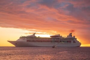 A majestic cruise ship sails across the Caribbean Sea at sunset in Grenada, showcasing a vibrant orange sky.